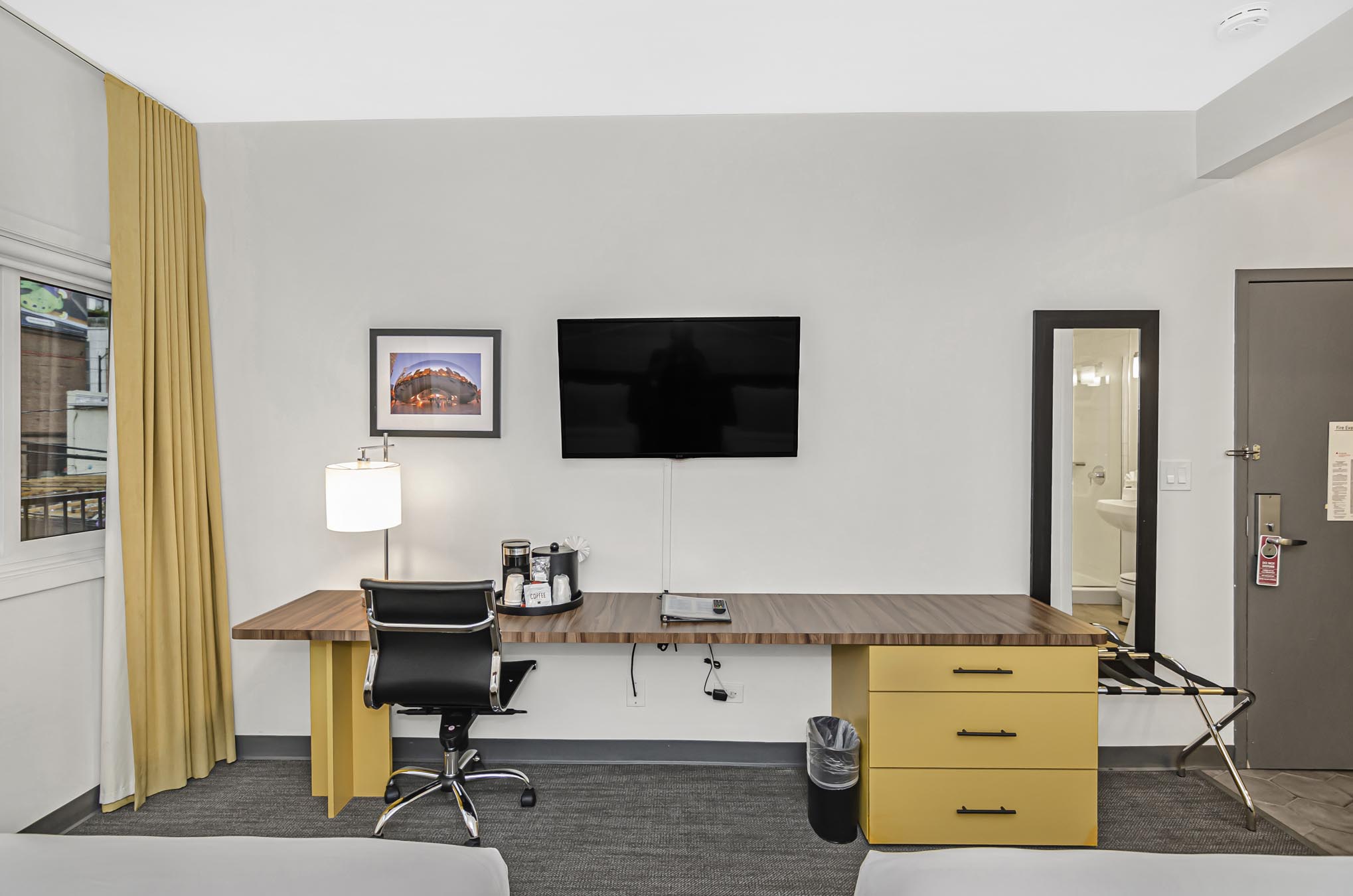 Mounted TV over work desk, swivel chair, and mirror on wall