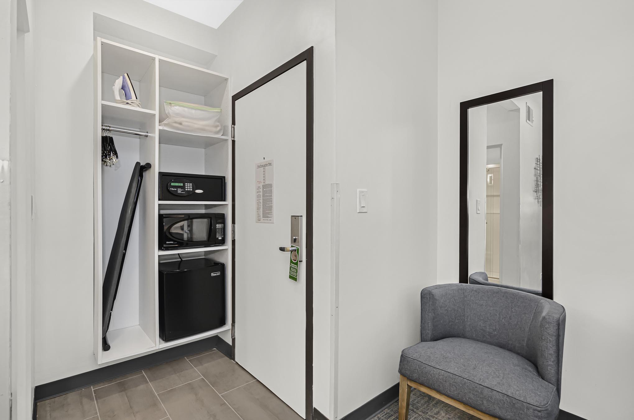 Grey chair with mirror hanging on wall, closet, microwave, safe, and