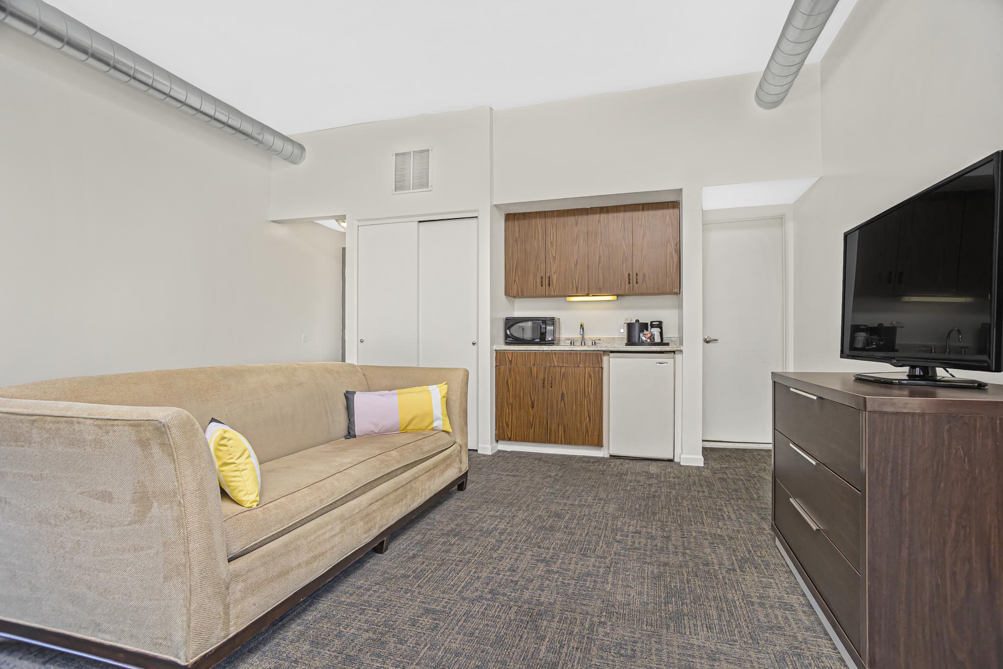Beige couch, TV, dresser, microwave, mini fridge, and closet